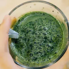 Zielony napój z bąbelkami, prawdopodobnie z dodatkiem chlorofilu, w szklance trzymanej w dłoni.