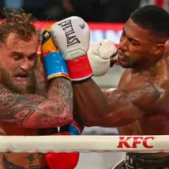 Two boxers grapple in the ring. One, with tattoos and wet hair, recoils from a punch. The other, muscular and focused, lands a blow. This is what heavyweight boxing looks like.