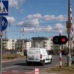 Czerwone światła na przejeździe kolejowym sygnalizują zatrzymanie. Znak informuje o przejściu dla pieszych i rowerzystów.