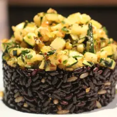 Riso nero compattato a cilindro, guarnito con un'abbondante porzione di zucchine saltate e erbe aromatiche.