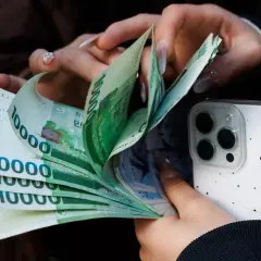 Dłonie liczą banknoty 10000 wonów, waluta Korei Południowej, obok białego etui na telefon.