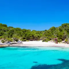 Aguas turquesas y arena blanca en la cala turqueta menorca, rodeada de pinos y rocas. Un paraíso balear.