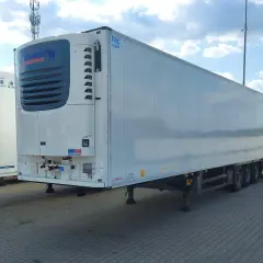 Biała naczepa chłodnia Schmitz Cargobull z niebieskim logo, zaparkowana na zewnątrz.