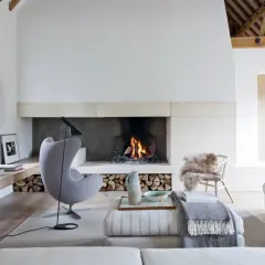 Acogedor salón con un mueble con chimenea encendida, sillón gris, sofás y decoración rústica.