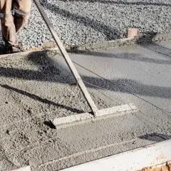 Un ouvrier lisse une **pente en béton** fraîchement coulée avec un râteau, créant une surface lisse pour une nouvelle construction.
