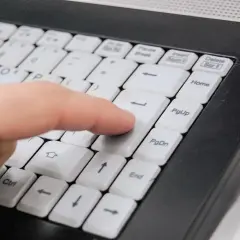 Palec naciska klawisz Enter na klawiaturze laptopa, symbolizując łatwy sposób, jak kupić prąd przez internet.