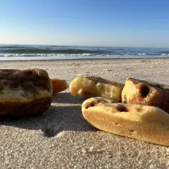 Kilka kawałków bursztynu leży na piaszczystej plaży, z morzem i błękitnym niebem w tle.