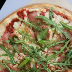 Pyszna pizza prosciutto z rukolą i sosem pesto.