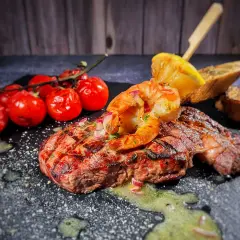 Perfektes Surf and Turf Rezept: saftiges Steak mit gegrillten Garnelen, Kirschtomaten und Zitronenspalte auf schwarzem Stein.