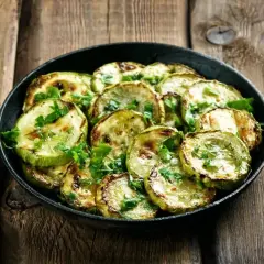 Zucchine marinate cotte, grigliate e guarnite con prezzemolo fresco, servite in una padella su un tavolo di legno rustico.