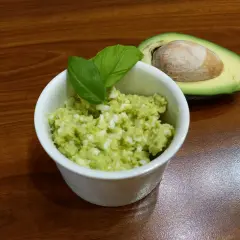 Pyszna pasta z awokado i jajka, udekorowana listkami bazylii, obok połówka awokado z pestką.