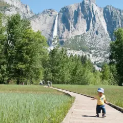 Mały chłopiec na ścieżce w Yosemite, w tle wodospad i trzy korony gór.
