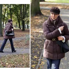 Kobieta w brązowej kurtce na zimę spaceruje po parku jesienią.