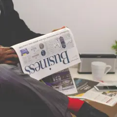 Mężczyzna w garniturze czyta gazetę "Business". Analizuje wykresy, zastanawiając się, czy akcje JSW pójdą w górę.