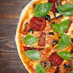 Pyszne rodzaje pizzy: z kiełbaską, boczkiem, pomidorami, oliwkami i bazylią na drewnianym tle.
