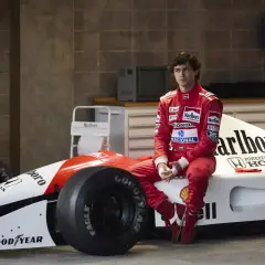 Młody kierowca w czerwonym kombinezonie siedzi na bolidzie F1. Czy to przyszły były brazylijski kierowca formuły 1?