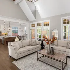 Stilvolles wohnzimmer einrichten mit beigen Sofas, Holzboden und offener Küche. Ein moderner Teppich und ein Couchtisch runden das Bild ab.
