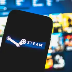 Smartfon z logo Steam na tle ekranu z grami. Zastanawiasz się, ile jest warte konto Steam?
