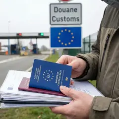Mężczyzna trzyma stos dokumentów, w tym europejską kartę broni, na tle granicy celnej UE.
