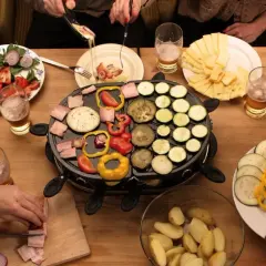Mesa con raclette, quesos, patatas, ensalada y muchas verduras para raclette: pimientos, calabacín, berenjena y tomate.