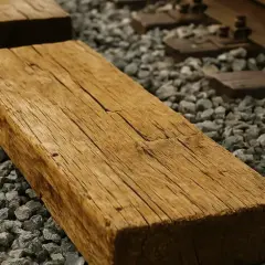 Stare, drewniane podkłady kolejowe czekają na utylizację. Widać szuter i fragmenty torów.