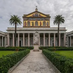 Il cortile della cattedrale San Paolo a Roma, con statue e palme, invita alla contemplazione.