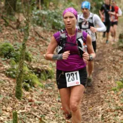 Une coureuse, dossard 231, s'élance sur un trail débutant en forêt. D'autres coureurs la suivent.