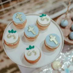 Jolis cupcakes décorés de croix dorées et de lettres pour un menu baptême à faire soi même. Des cake pops bleus sont aussi visibles.