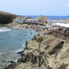 Gente disfrutando en un restaurante de Cabo de Gata, con vistas a una playa concurrida y el mar azul.