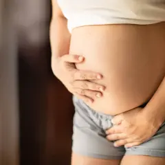 Brzuch kobiety w ciąży, która odczuwa częste oddawanie moczu w ciąży 1 trymestr. Dłonie obejmują zaokrąglony brzuch.