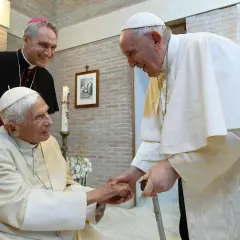 Papst Franziskus und ein Bischof besuchen Papst Benedikt. Sie reichen sich die Hände und lächeln.