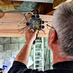 Elektryk kończy instalację elektryczną w garażu, łącząc przewody w puszce.