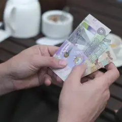 Dłonie trzymają banknoty, które mogą być najdroższą walutą świata. W tle biały czajniczek i filiżanka kawy.