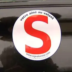 Macaron "votre aîné au volant" sur une voiture. Le S rouge est bien visible.