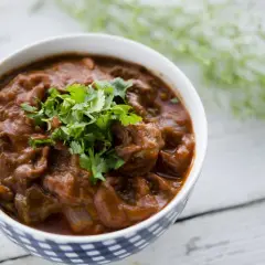 Miseczka z gęstym, pomarańczowym gulaszem tikka masala, ozdobiona świeżą kolendrą.