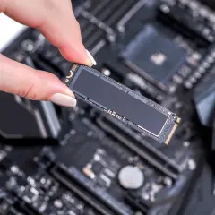 Eine Hand hält eine M.2 SSD, bereit für den Einbau in einen SSD-Steckplatz auf einem Computer-Motherboard.