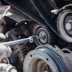 Mano enguantada ajusta la correa de distribución de un coche con una llave de carraca.
