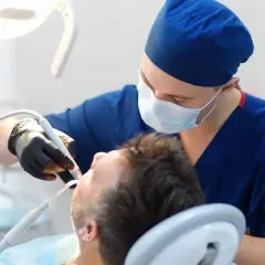 Dentysta w masce i rękawiczkach wykonuje zabieg. Sen o dentystach może oznaczać troskę o zdrowie lub potrzebę zmian.