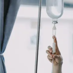 Dłoń reguluje kroplówkę, łagodząc ból po chemioterapii. W tle zasłona i okno.