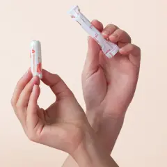 Zwei Hände halten Tampons. Einer ist ausgepackt, der andere noch in seiner Hülle. So sieht ein Tampon aus.