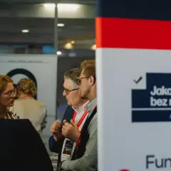 Ludzie rozmawiający na tle banera z napisem "Jakość bez retuszu".