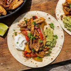 Färdiglagade fajitas med kyckling, paprika och lök på tortillabröd, serverade med guacamole och gräddfil. Ett perfekt fajitas recept för en härlig middag.