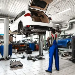 Mechanik zastanawia się, ile kosztuje założenie warsztatu samochodowego, patrząc na podniesione auto i części na podłodze.