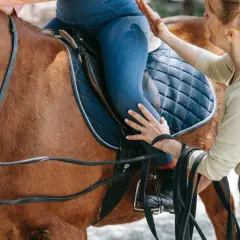 Instruktorka pomaga jeźdźcowi na koniu, trzymając wodze.