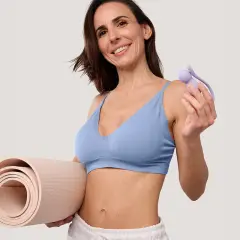 Une femme souriante tient un accessoire pour muscler son périnée à 60 ans et un tapis de yoga.