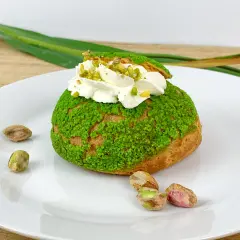 Pyszne ptysie z kremem pistacjowym, posypane zielonymi okruszkami i orzechami.