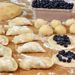 Przygotowania do tego, jak zrobić pierogi z jagodami: ciasto, kulki ciasta, gotowe pierogi i te w trakcie lepienia z jagodami.