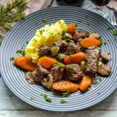 Herzhaftes Boeuf Bourguignon Rezept: zartes Rindfleisch mit Karotten, Pilzen und Kartoffelpüree auf einem grauen Teller, garniert mit Petersilie.