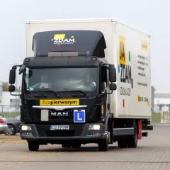 Ciężarówka szkolna z napisem "JA ZDAM SZKOŁA JAZDY" i tablicą "L" na masce. Kierowca zdobywa doświadczenie do prawa jazdy C+E.