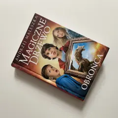 Okładka książki "Magiczne drzewo. Obrońca" z Andrzejem Maleszką. Trójka dzieci patrzy z zaciekawieniem na smoka w ramie.
